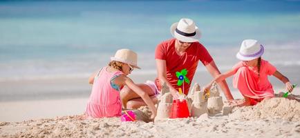 padre y dos niñas jugando con arena en la playa tropical foto