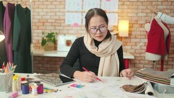 Asian middle-aged female fashion designer and young trainee tailor work in a studio with colorful thread and sewing fabric for a dress design collection ideas, professional boutique small business.