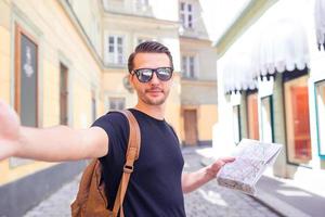 Man tourist with a city map and backpack in Europe street. Caucasian boy looking with map of European city. photo