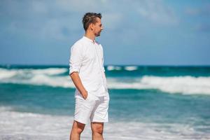 Young man in white walking on the beach photo