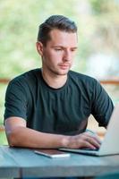 joven con laptop en café al aire libre tomando café. hombre usando teléfono inteligente móvil. foto