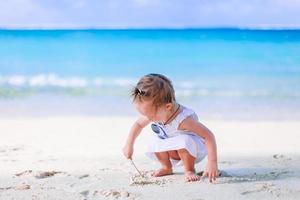 Little girl at tropical white beach making sand castle photo