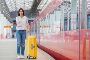 mujer joven con equipaje en una estación de tren. turista caucásica esperando su tren expreso mientras viaja. foto
