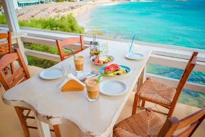 Traditional lunch with delicious fresh greek salad, frappe and brusketa served for lunch at outdoor restaurant with beautiful view on the sea and port photo