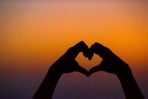 Silhouette of heart made hands at sunset photo