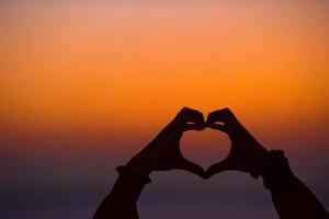 Silhouette of heart made hands at sunset photo