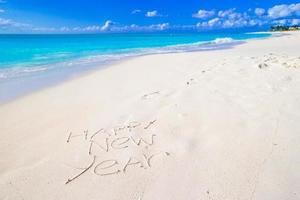 feliz año nuevo escrito en la playa de arena blanca con sombrero rojo de santa foto