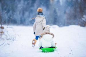 Little adorable girls enjoy a sleigh ride. Child sledding. Children play outdoors in snow. Family vacation on Christmas eve outdoors photo