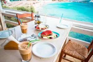 Traditional dinner with delicious fresh greek salad, frappe and brusketa served for lunch at outdoor restaurant with beautiful view on the sea and port photo