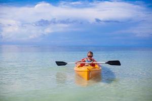 pequeña niña valiente y linda flotando en un kayak sola en el mar azul alto foto