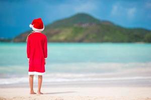 Adorable niña con gorro de Papá Noel en la playa tropical foto