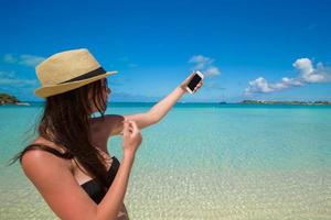 mujer joven toma una foto en su teléfono en la playa tropical