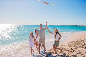 Happy young family with two kids with flying a kite on the beach photo
