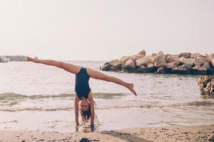 niña activa en la playa divirtiéndose mucho. lindo niño haciendo ejercicios deportivos en la orilla del mar foto