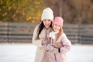 Little adorable girl with her mother skating on ice-rink photo