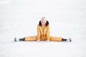 adorable niña sentada en el hielo con patines después de la caída foto