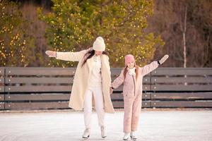 Little adorable girl with her mother skating on ice-rink photo