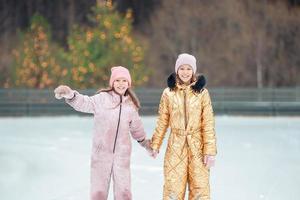 chicas adorables patinando en la pista de hielo al aire libre en el día de nieve de invierno foto