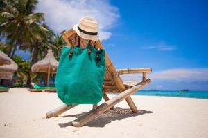 Wooden beach chair with hat and bag on white sand beach photo