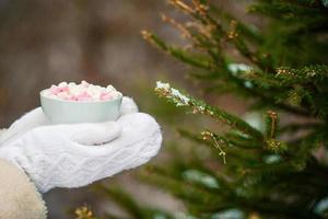 Female hands holdink white cup of coffee with white and pink marshmallows photo