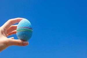 hermoso y brillante huevo de pascua en la mano sobre el fondo del cielo azul foto