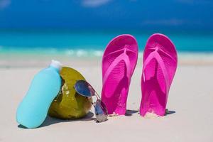 Flip flops, coconut and suncream on white sand photo