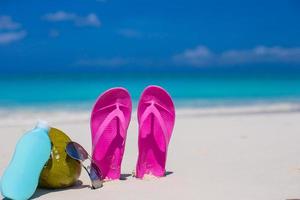 Flip flops, coconut and suncream on white sand photo