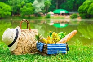 cesta de picnic con frutas, pan y sombrero en bolsa de paja foto