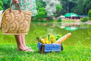 cesta de picnic con frutas, pan y sombrero en bolsa de paja foto