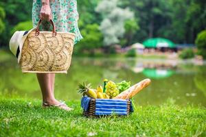 cesta de picnic con frutas, pan y sombrero en bolsa de paja foto