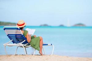 Young woman reading book on chaise-lounge on the beach photo