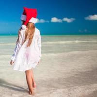 Little adorable girl in red Santa hat at tropical beach photo