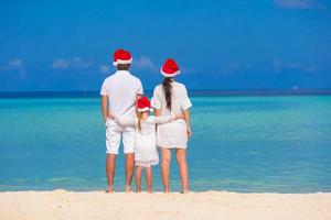 familia feliz de tres en sombreros de santa en la playa foto