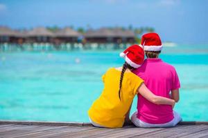 Vista trasera de una pareja joven con sombreros de Papá Noel en un embarcadero de madera en vacaciones de Navidad foto
