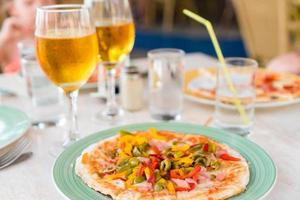 Pizza with mozzarella cheese, olive, fresh tomato and pesto sauce. Served at restaurant table with two beers photo