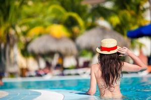 hermosa joven relajándose en la piscina. vista trasera de una chica en la piscina al aire libre en un hotel de lujo foto