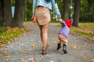 vista trasera de la joven madre caminando con su pequeña hija en el parque de otoño