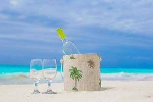 botella de vino blanco y dos copas en la exótica playa de arena foto