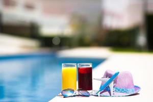 Glasses of juice, straw hat, sunglasses and airplane model on summer vacation near swimmingpool photo