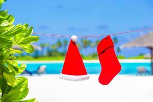 Red Santa hat and Christmas stocking between palm trees photo