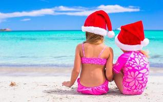 Little adorable girls in Santa hats during beach vacation photo