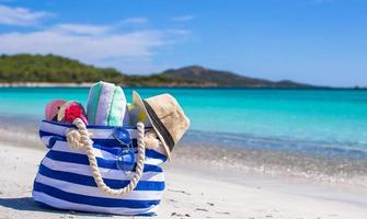 Blue bag, straw hat, flip flops and towel on white beach photo