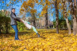 adorable niñita con papá feliz divirtiéndose en el parque de otoño en un día soleado foto