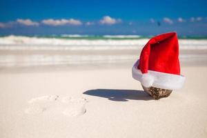 Santa Claus hat at coconut on a white sandy beach photo