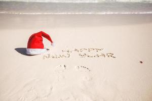 feliz año nuevo escrito en la arena y gorro de Papá Noel en la playa de arena blanca foto