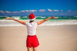 Young woman in Santa Hat walking spread her hands on white sandy beach photo