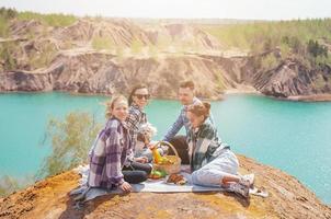 Young parents and kids on picnic after hiking in mountains. Beautiful view of blue lake photo