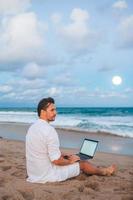 Man with laptop on the beach at sunset photo