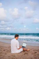 hombre con laptop en la playa al atardecer foto