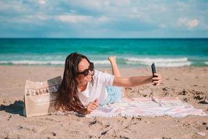 Happy young woman relaxing on the beach and taking selfie picture by smartphone photo